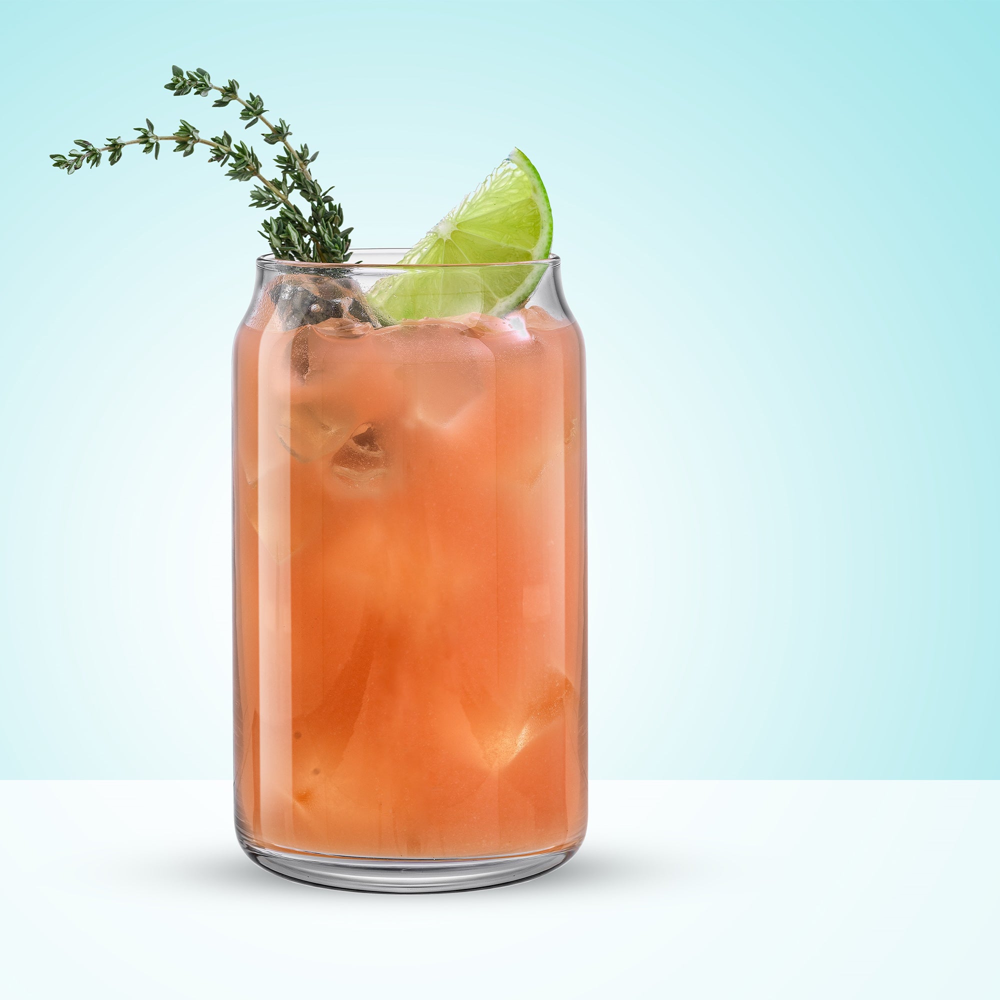 A glass of orange drink with a sprig of thyme, served in a Classic Can Shape Tumbler Drinking Glass Cup by JoyJolt.
