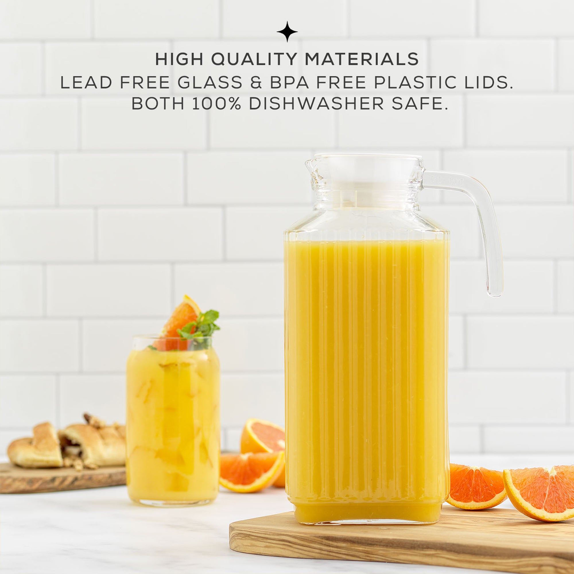 A 60-ounce JoyJolt Beverage Serveware Glass Pitcher filled with orange juice sits on a table. The pitcher has a clear glass body and a handle for easy pouring. Text on the image reads “HIGH QUALITY MATERIALS. LEAD FREE GLASS & BPA FREE PLASTIC LIDS. BOTH 100% DISHWASHER SAFE.”
