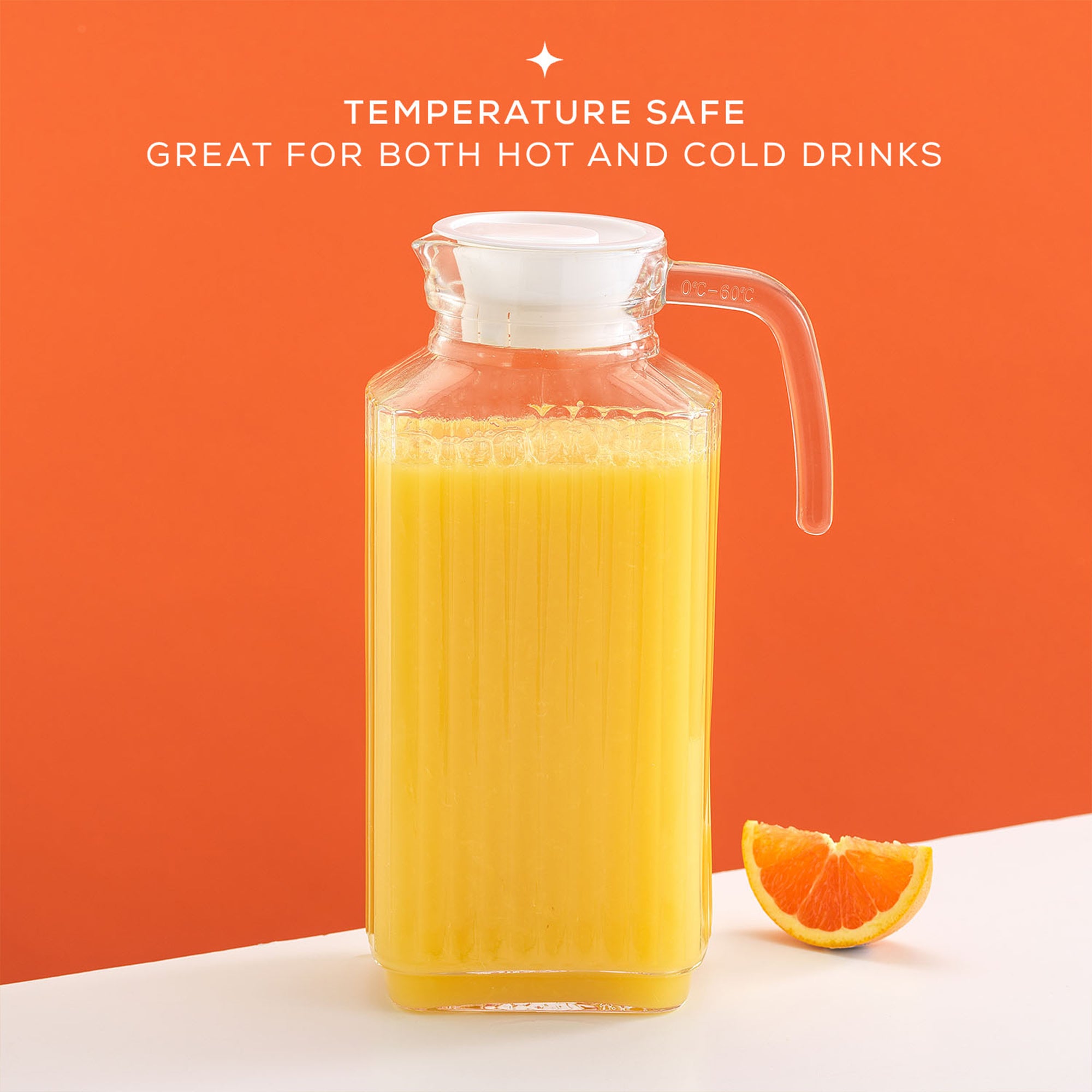 A 60-ounce JoyJolt Beverage Serveware Glass Pitcher filled with orange juice sits on a table next to a single orange. The pitcher has a clear glass body and a handle for easy pouring. Text on the image reads "TEMPERATURE SAFE. GREAT FOR BOTH HOT AND COLD DRINKS".