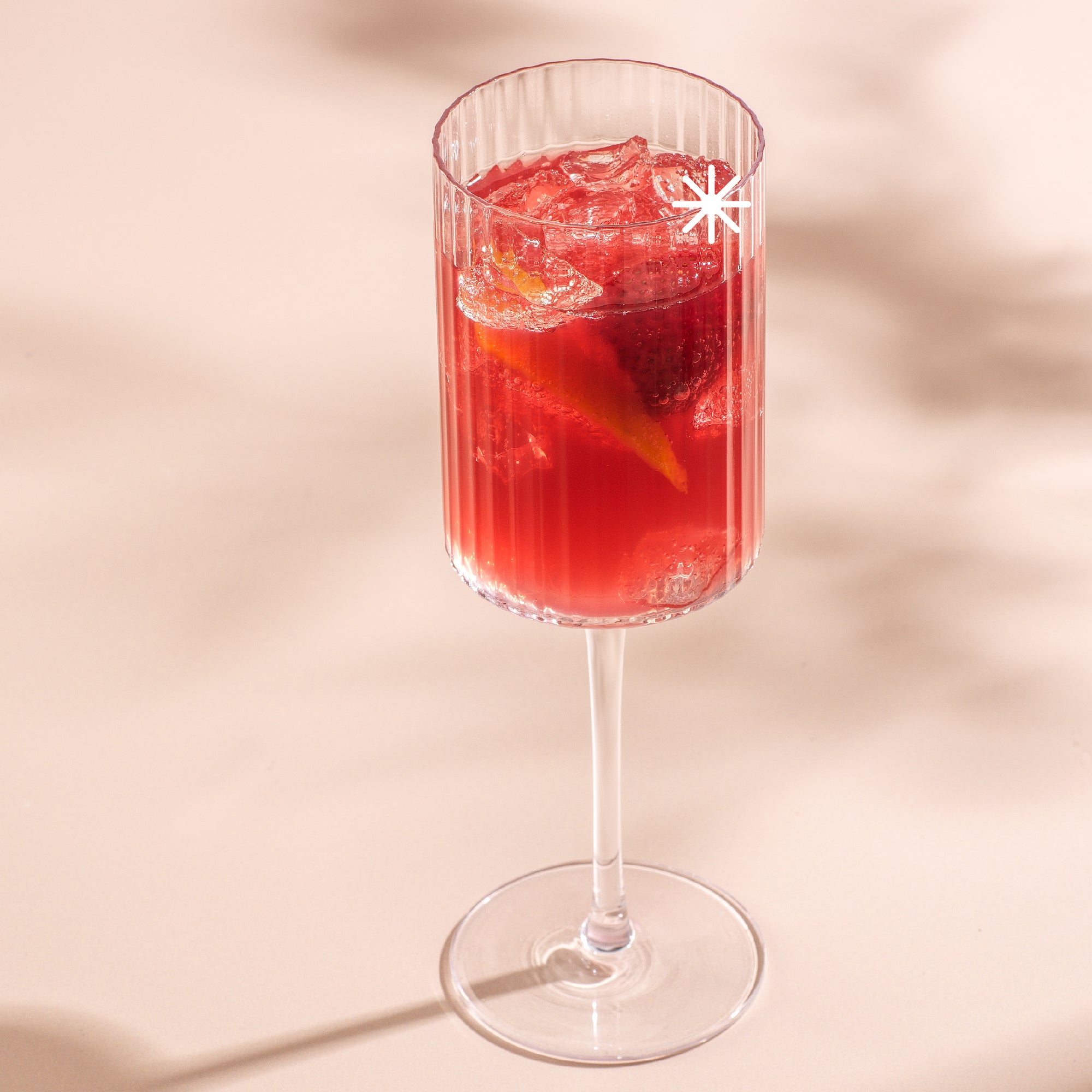 A tall, stemmed glass filled with a refreshing red cocktail. The drink is garnished with a lemon wedge and strawberries, and contains ice cubes.