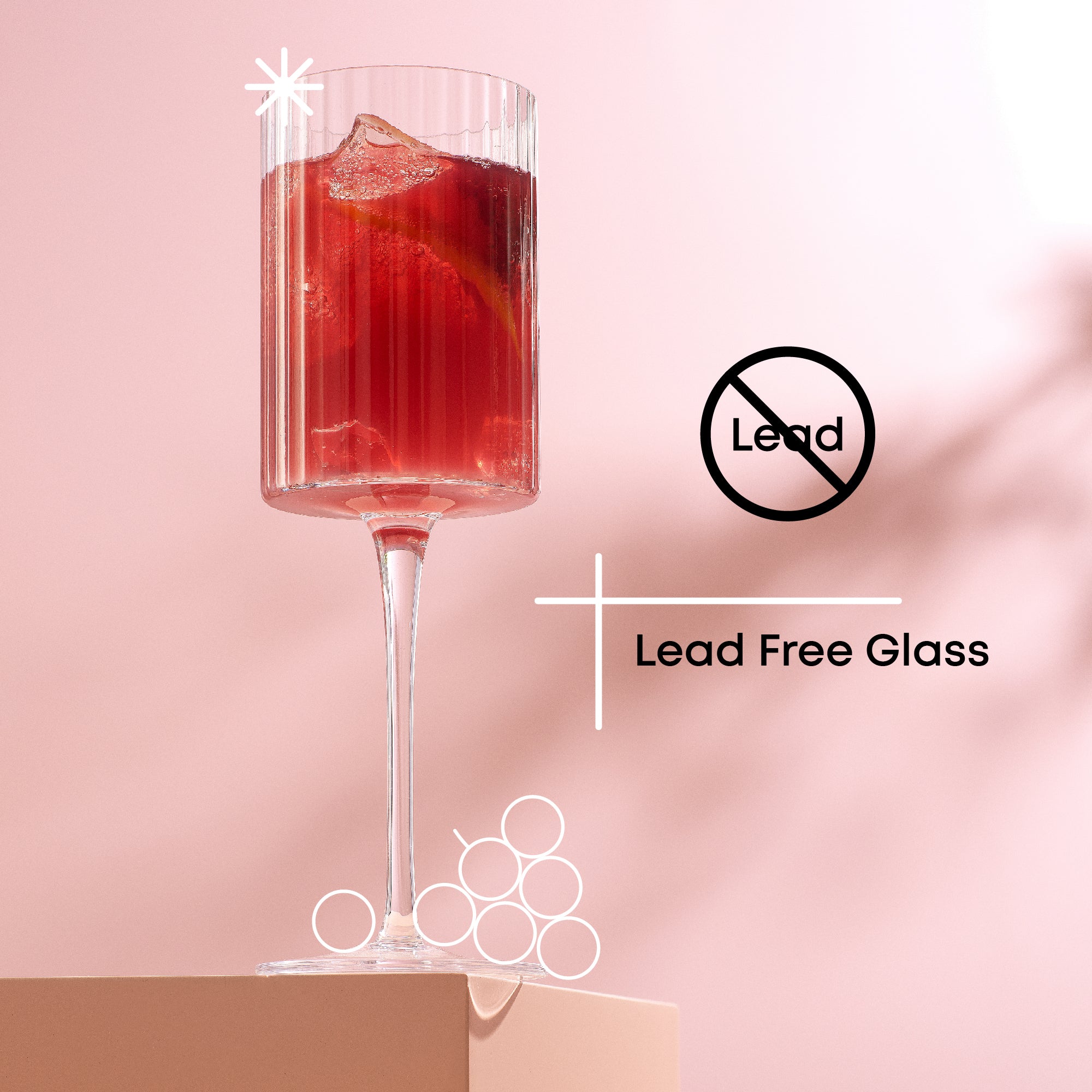 A tall, stemmed glass filled with a red cocktail. The background is pink. Text on the right reads "Lead Free" with a slash through a lead symbol, and "Lead Free Glass."