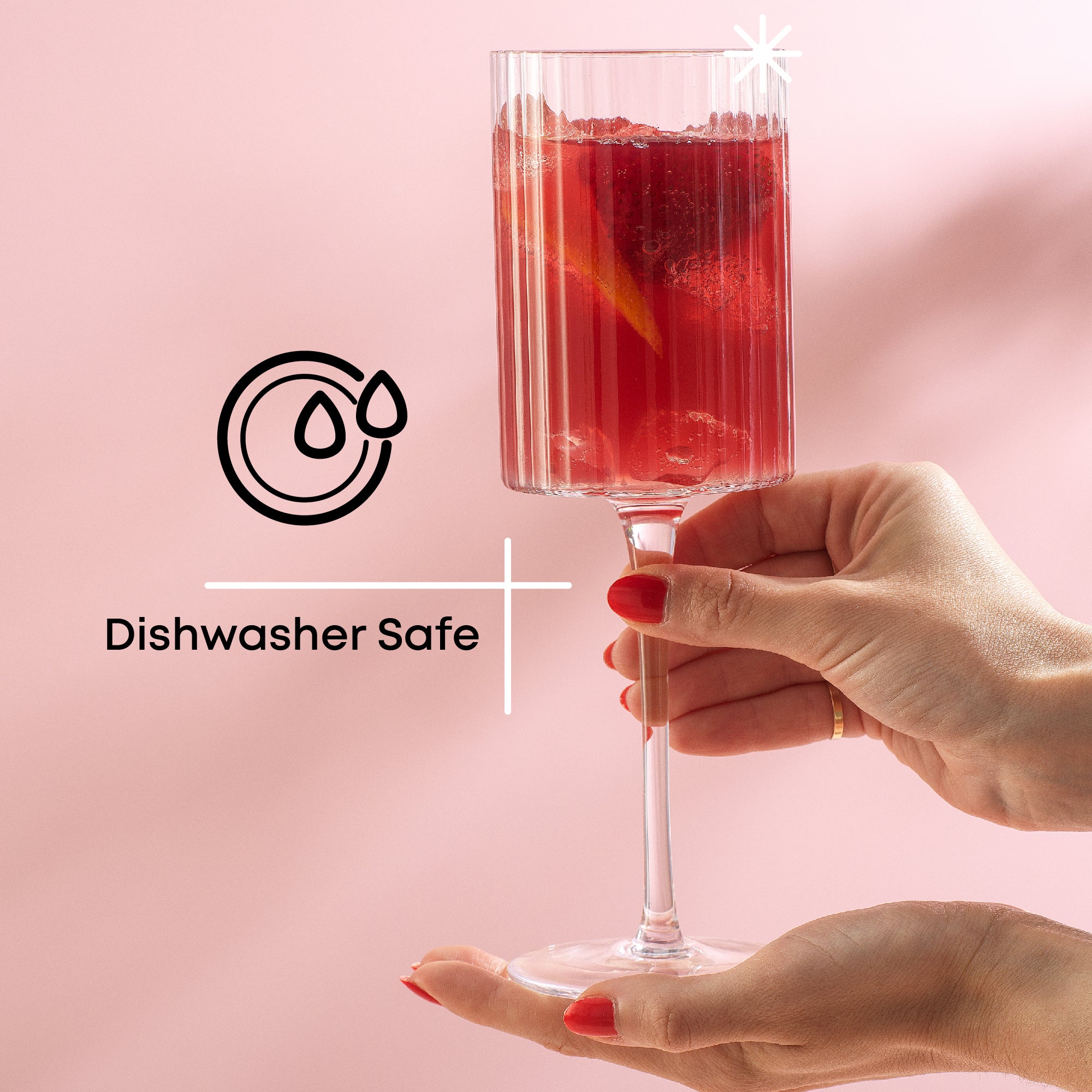 A hand holds a tall, stemmed glass filled with a red cocktail. The background is pink. Text on the right reads "Dishwasher Safe" with a dishwasher symbol.