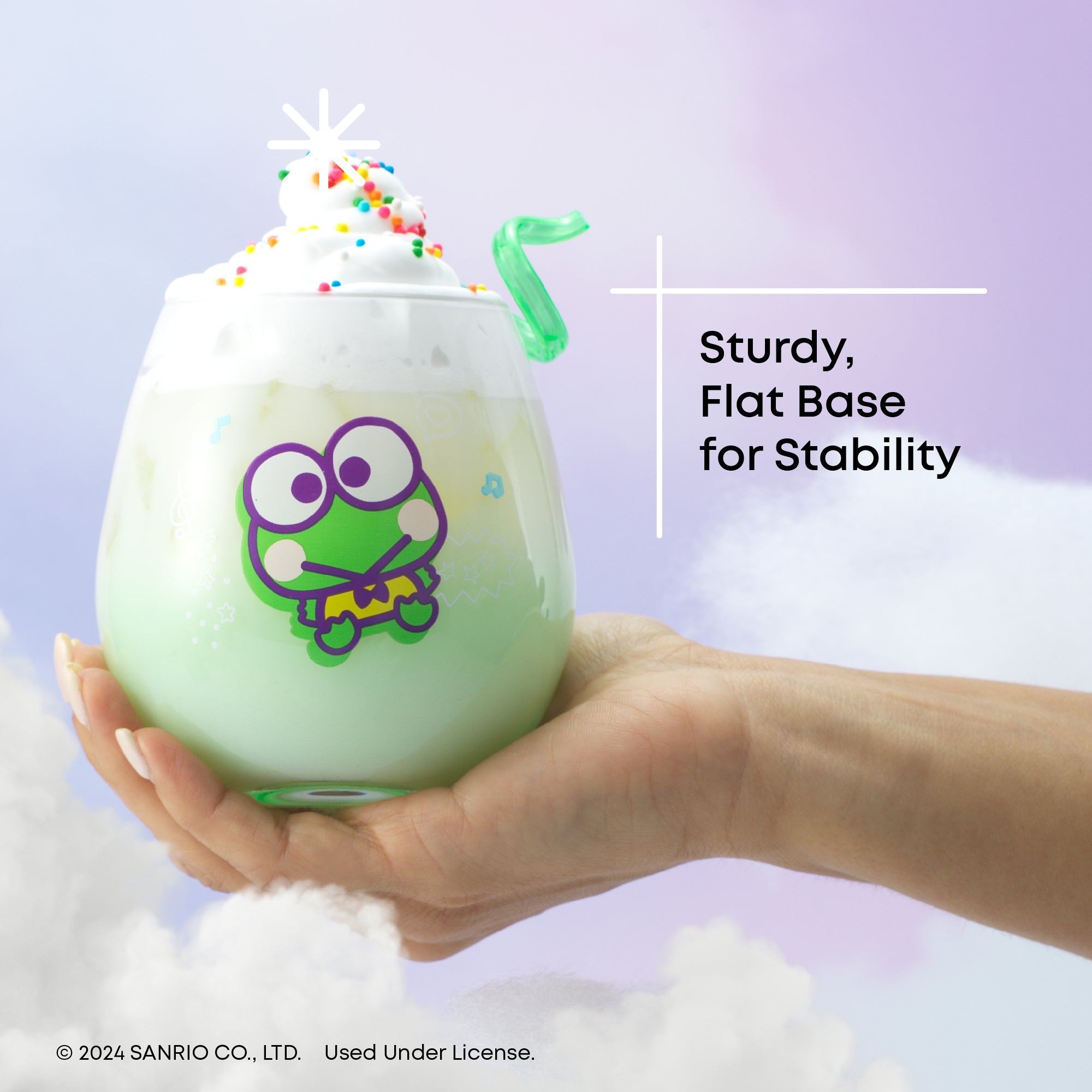 A hand holding a green ombre Hello Kitty and Friends glass featuring Keroppi. The glass is filled with a green drink topped with whipped cream and sprinkles.