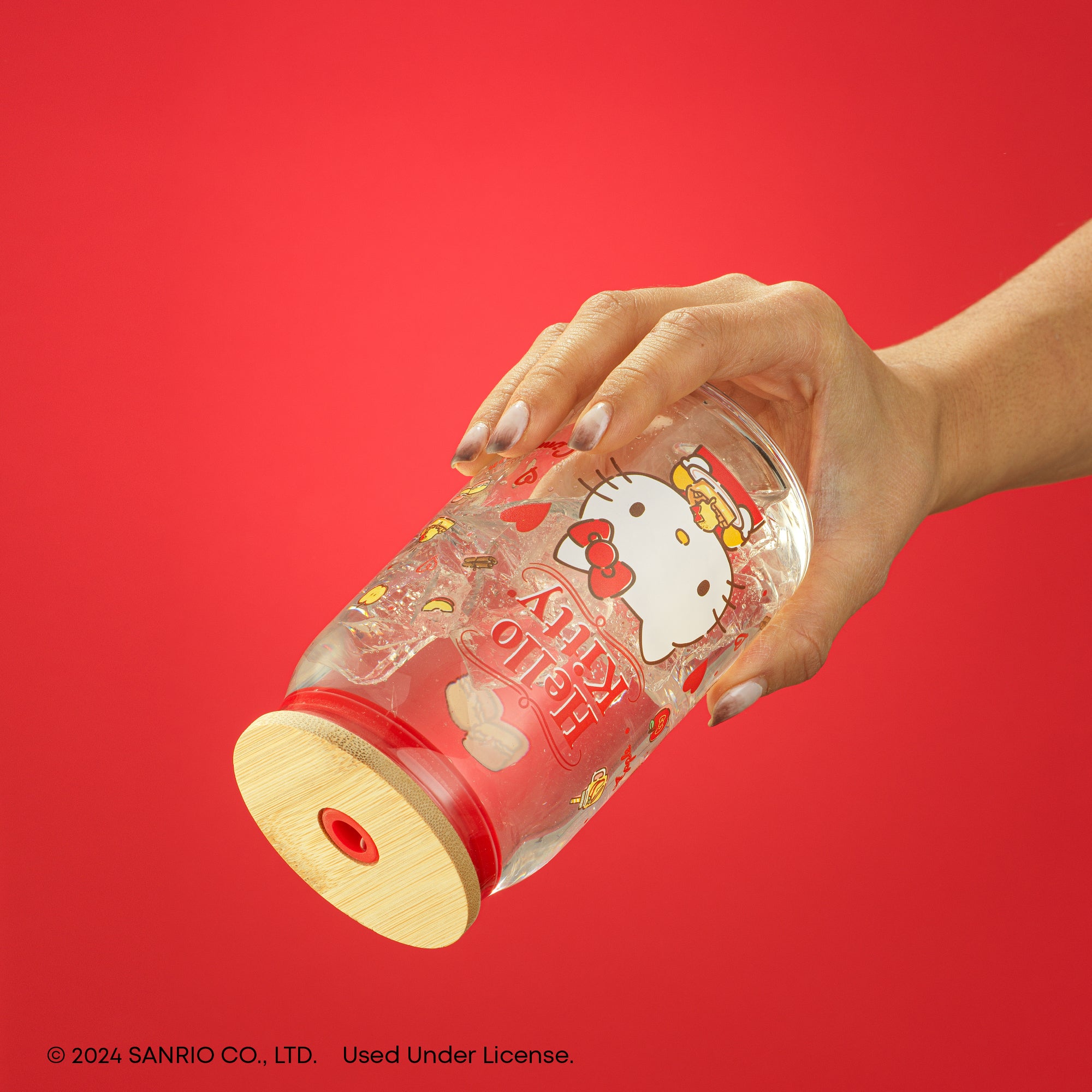 A person holding a Hello Kitty tumbler glass with a bamboo lid. 