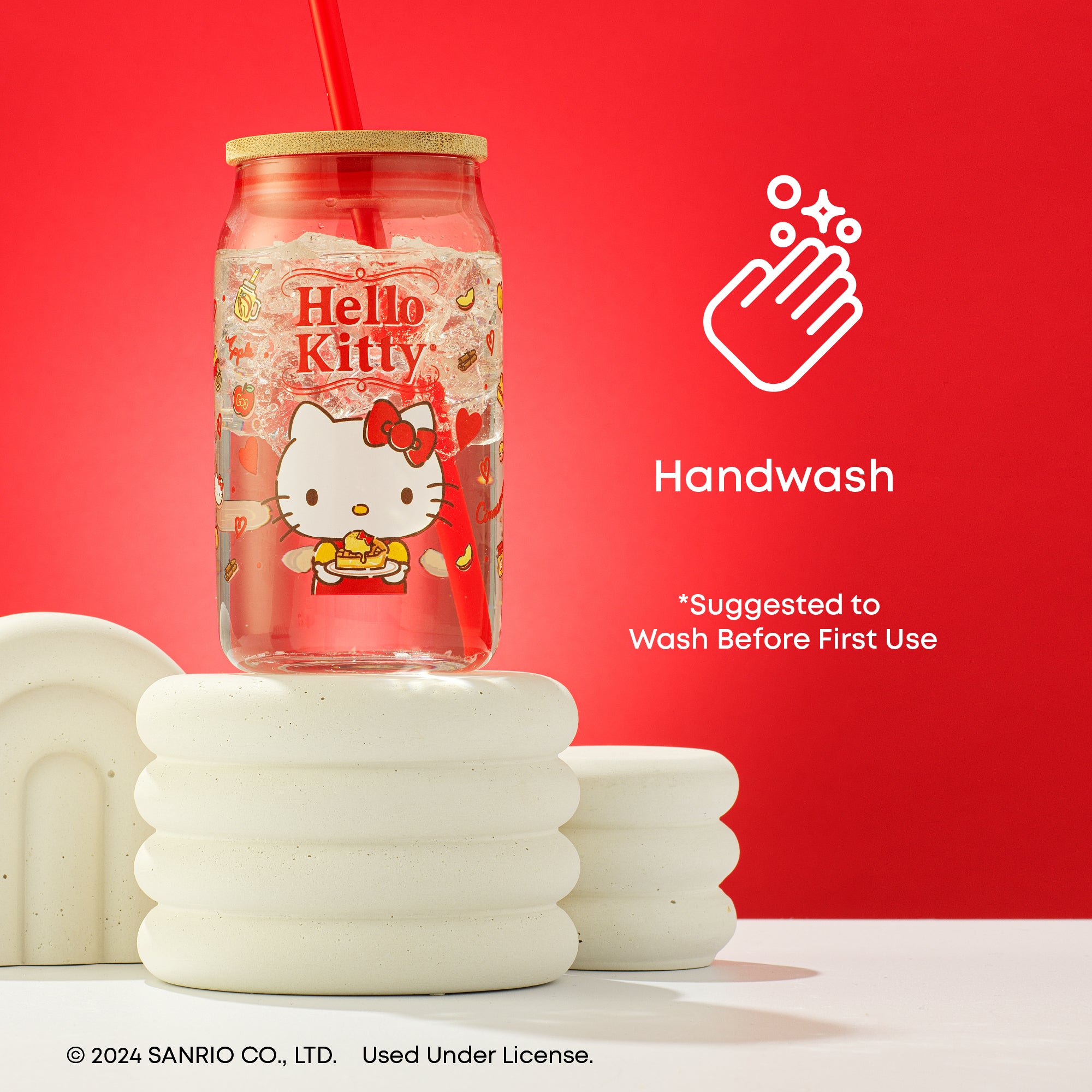 A JoyJolt x Hello Kitty tumbler with bamboo lid and straw sitting on top of a stack of white decorative. Text on the image reads "Handwash. Suggested to wash before first use." 