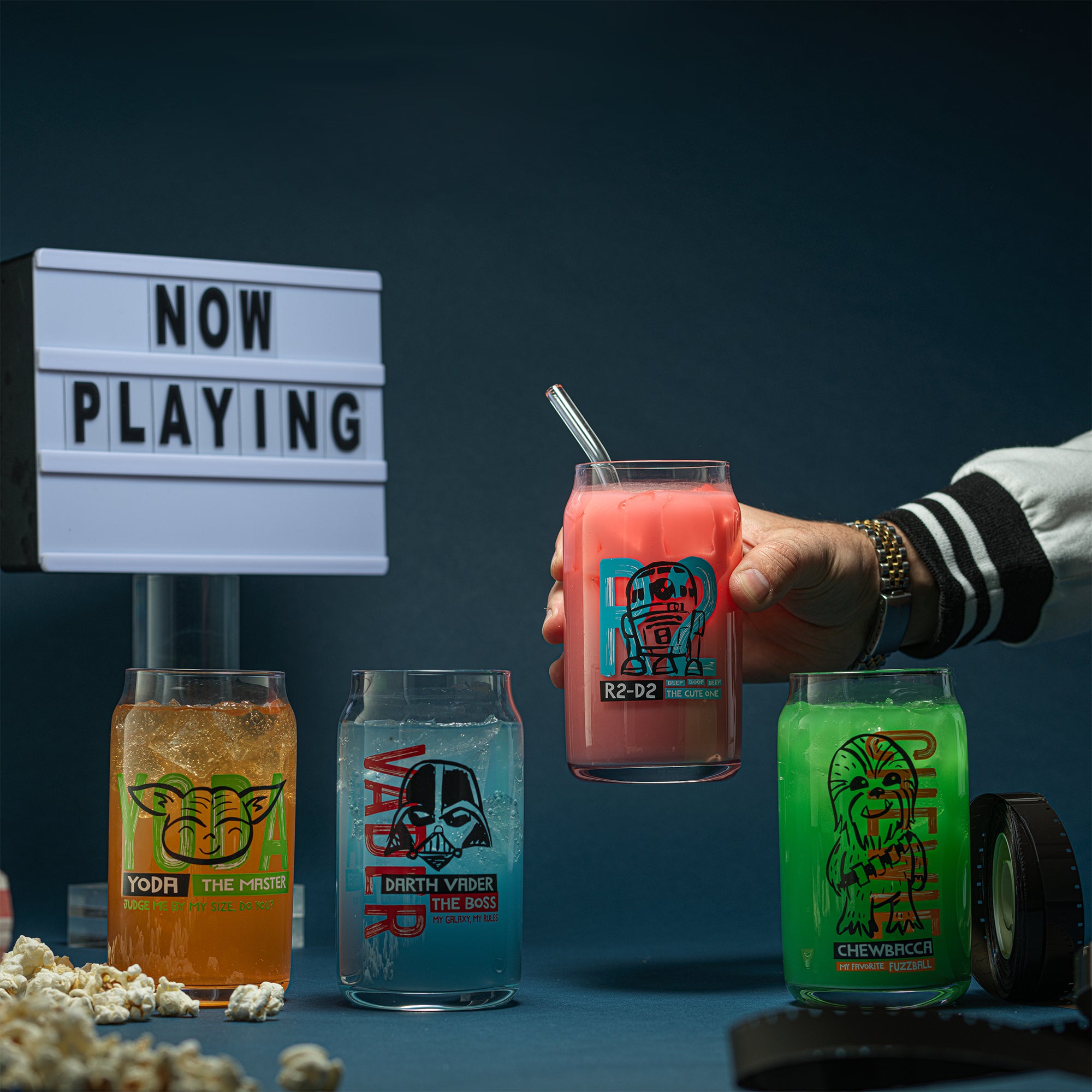 JoyJolt's Star Wars 'Now Playing' glass tumbler set. A 'Now Playing' movie sign in the background and some popcorn around the glasses. 